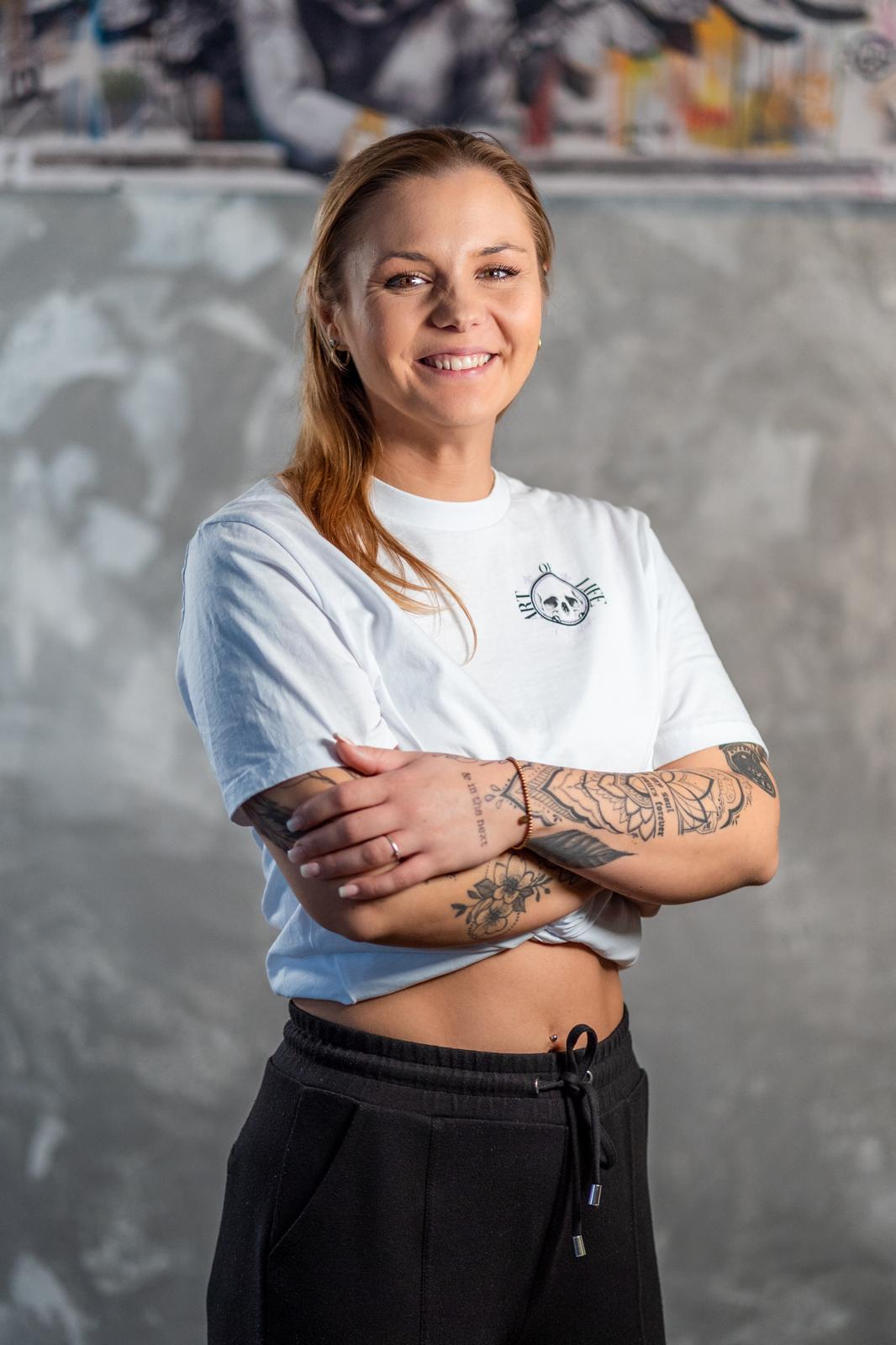 Livia, Founder und Head Artist von Art of Life, lächelnd mit verschränkten Armen im Studio